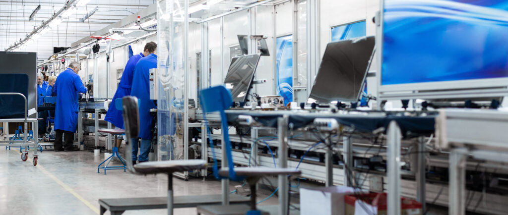 Elektronik fabrikasında işçiler mavi önlüklerle üretim hattında çalışıyor.