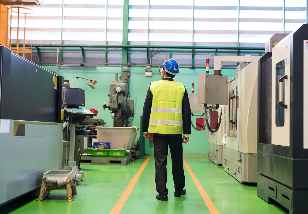 Fabrika tesisinde iş güvenliği mühendisi, makineler arasında inceleme yapıyor.