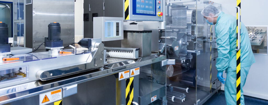 İlaç üretim bandında hijyenik kıyafetli personel makineyi kontrol ediyor.