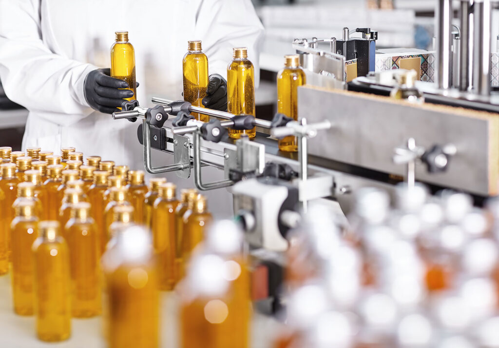 Beyaz önlüklü işçi üretim hattında şişelere sıvı ürün dolduruyor.