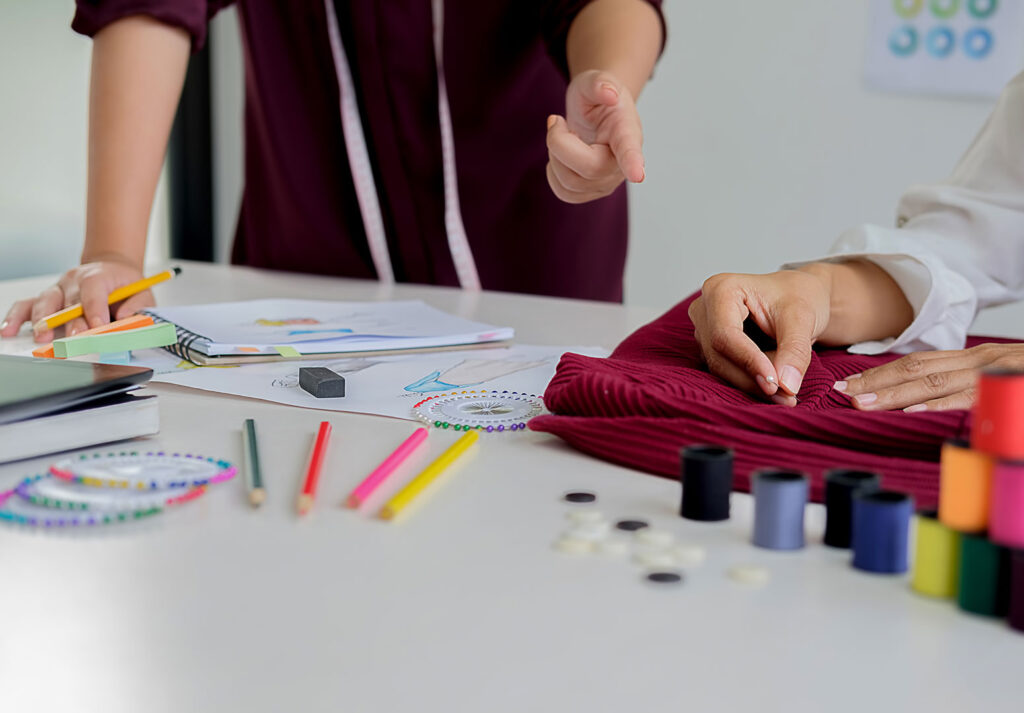 Moda tasarım atölyesinde çalışanlar, kumaş ve tasarım çizimleri üzerinde çalışıyor.