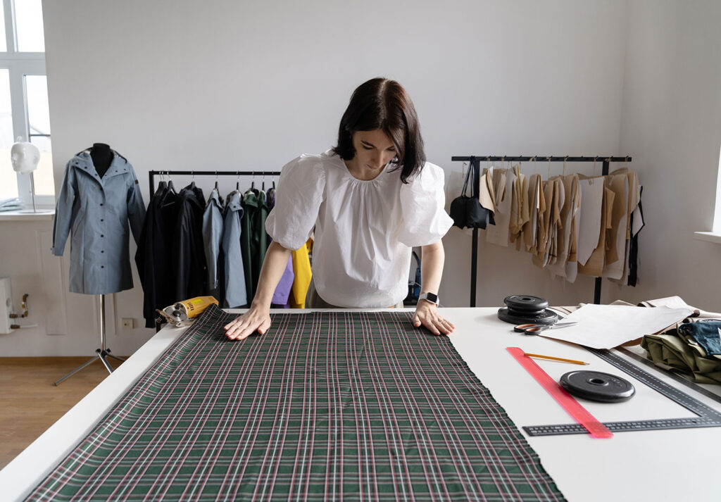 Moda tasarımcı atölyesinde kadın çalışan kumaş üzerinde ölçüm yapıyor.