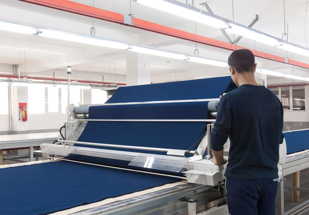 Tekstil fabrikasında çalışan, mavi kumaş üretim makinesini kontrol ediyor.