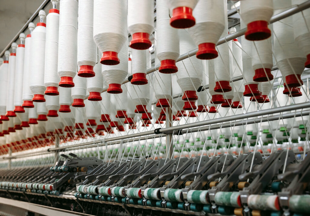 Tekstil fabrikasında beyaz iplik bobinleri üretim hattında dizili.