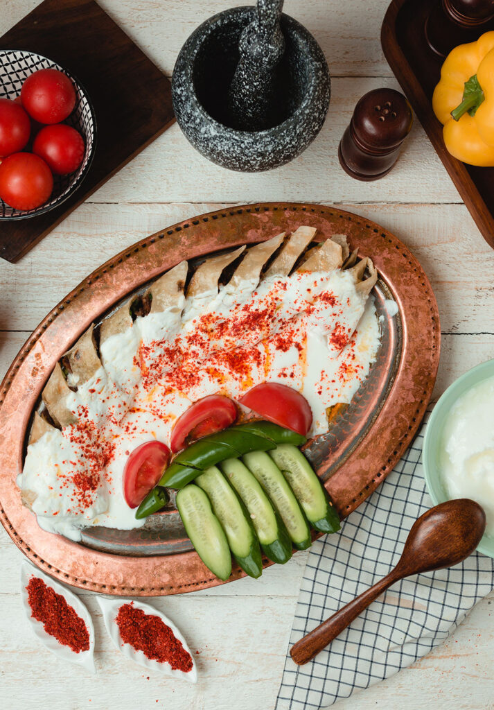 Bakır tabakta yoğurtlu et yemeği, salatalık ve domates sunumu – yemek fotoğraf çekimi